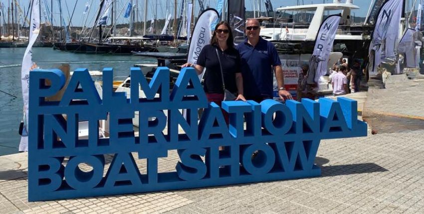 Marie and Nic from Triangle Berth Brokers standing behind a blue signs for Palma International Boat Show